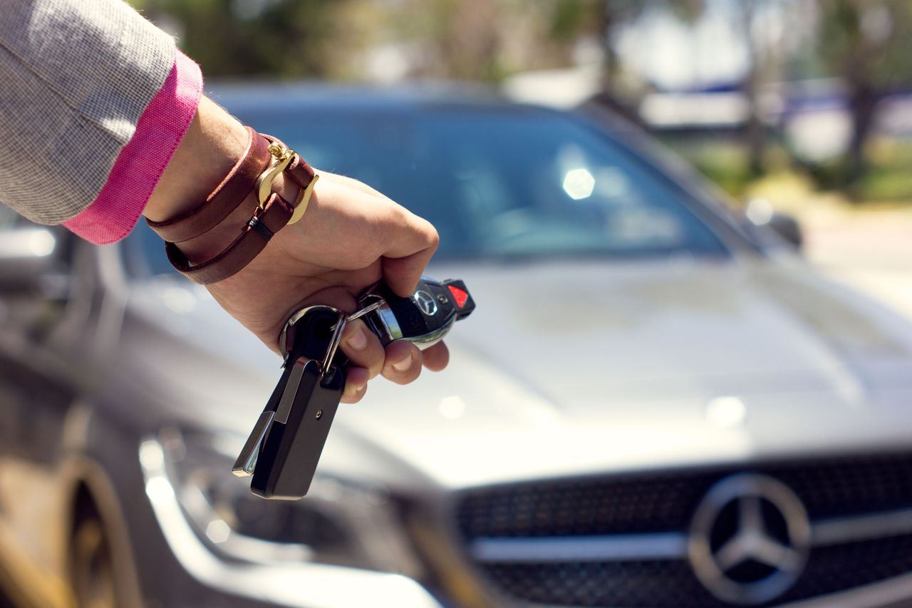 A close-up image of a hand holding car keys against the backdrop of a luxury car, outdoors.